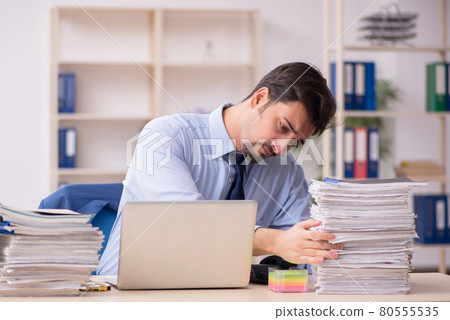 Young male employee and too much work in the office Young male employee and too much work in the office 80555535