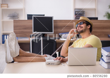 Young male employee preparing for trip at workplace Young male employee preparing for trip at workplace 80556280