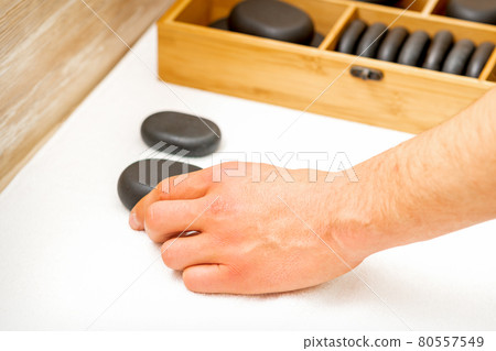 Hand of masseur takes black massage stones from the table in spa salon. 80557549