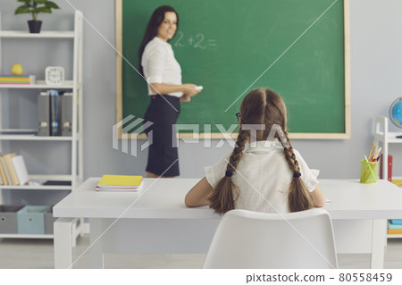Schoolkid sitting at desk and listening attentively to teacher in modern classroom 80558459