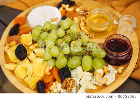 cheeses with grapes, dried fruits, nuts, honey and jam on a round wooden plate. 80558565