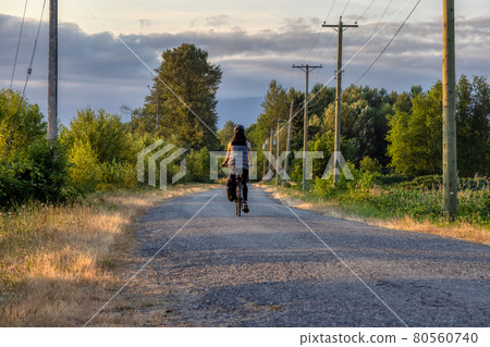 Adventurous White Cacasusian Woman riding a bicycle on a road. Adventurous White Cacasusian Woman riding a bicycle on a road. 80560740