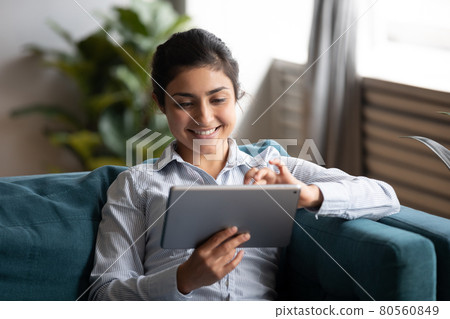 Happy indian woman using tablet sit on sofa at home Happy indian woman using tablet sit on sofa at home 80560849