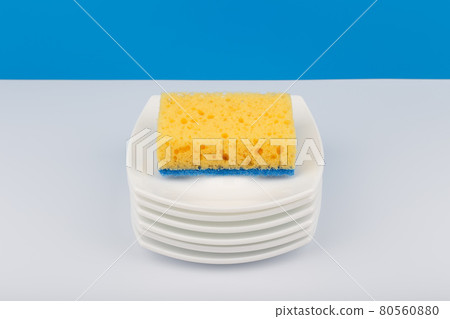 Dishwashing concept, high angle view of cleaning sponge on pile of clean saucers on white table with blue background Dishwashing concept, high angle view of cleaning sponge on pile of clean saucers on white table with blue background 80560880