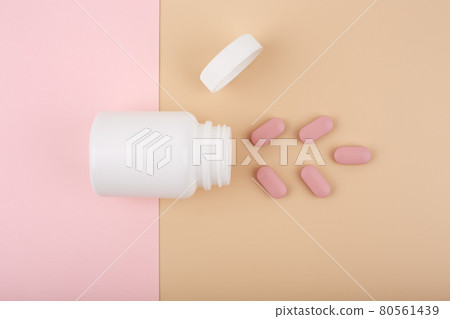 White opened medication bottle with pink spilled pills against pastel pink and beige background White opened medication bottle with pink spilled pills against pastel pink and beige background 80561439
