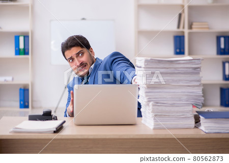 Young male employee unhappy with excessive work in the office Young male employee unhappy with excessive work in the office 80562873