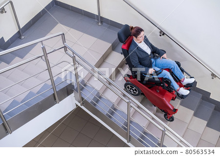 Caucasian woman in wheelchair with electric caterpillar going down stairs. 80563534