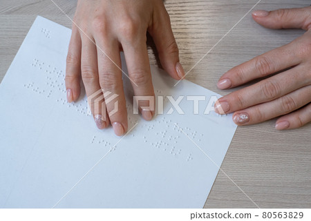 Close-up woman reads the text to the blind. Woman's hands on paper with braille code. 80563829