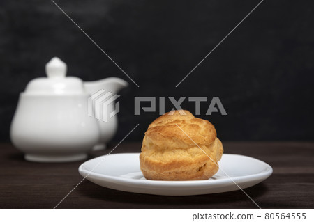 Homemade profiterole, puff, popover, eclair on white plate on teapot background. Close up dessert Homemade profiterole, puff, popover, eclair on white plate on teapot background. Close up dessert 80564555