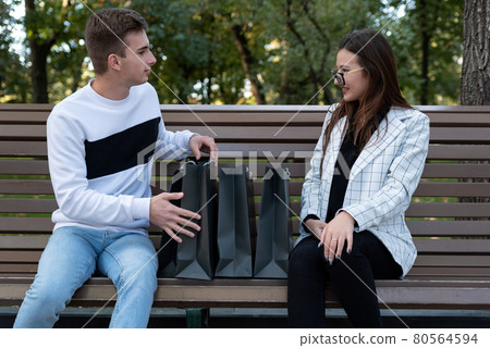 Young man and woman after day shopping is resting on bench in park. Couple with shopping bags consider shopping 80564594