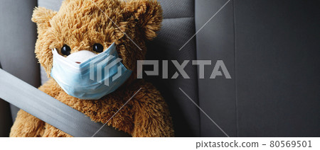 A brown teddy bear wearing a mask sits in the car. A brown teddy bear wearing a mask sits in the car. 80569501