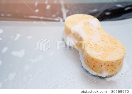 Yellow sponge and soap over the car for washing. Motor hood being cleaned. Concept car wash clean. Leave space for writing messages. Yellow sponge and soap over the car for washing. Motor hood being cleaned. Concept car wash clean. Leave space for writing messages. 80569970