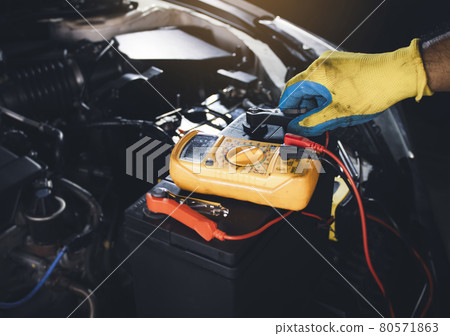 Technician clamping jumper cable for checking car battery voltage with digital multimeter 80571863