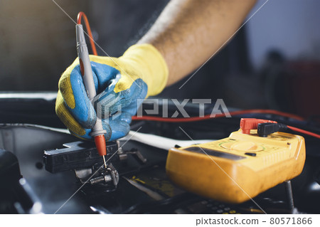 Technician checking car battery voltage with digital multimeter probe 80571866