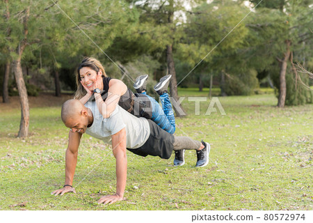 Fitness couple doing push-ups in the park. Woman on back of man Fitness couple doing push-ups in the park. Woman on back of man 80572974
