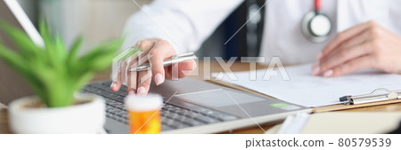 Doctor holds pen and works on laptop in medical office 80579539
