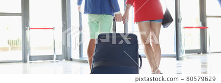 Man and woman are rolling suitcase towards exit of building Man and woman are rolling suitcase towards exit of building 80579629