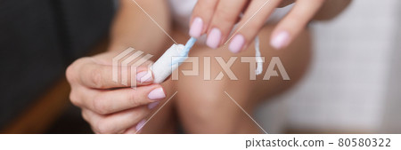 Woman in restroom sits on toilet and holds hygienic tampon in her hands 80580322