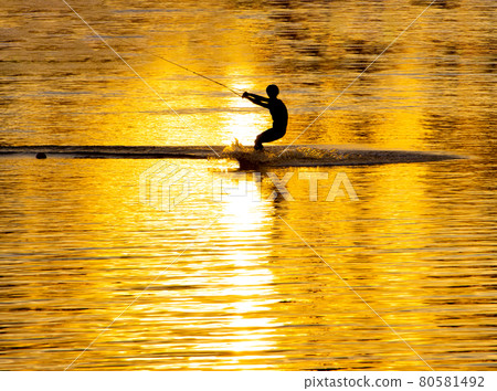 Silhouette of an athlete riding a water ski at sunset Silhouette of an athlete riding a water ski at sunset 80581492