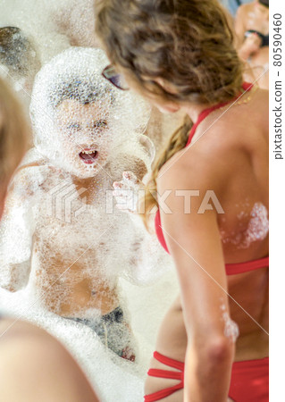 Young boy at the foam party. The face and body are covered with foam. Holiday concept. Young boy at the foam party. The face and body are covered with foam. Holiday concept. 80590460