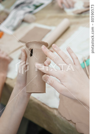 Women's hands knead clay, drawing elements of the product. Production of ceramic products at the master class on ceramics. Women's hands knead clay, drawing elements of the product. Production of ceramic products at the master class on ceramics. 80590573