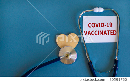 Covid-19 vaccinated symbol. White card with words 'Covid-19 vaccinated' and stethoscope on blue background. Wooden heart. Medical and covid-19 vaccinated pandemic concept, copy space. Covid-19 vaccinated symbol. White card with words 'Covid-19 vaccinated' and stethoscope on blue background. Wooden heart. Medical and covid-19 vaccinated pandemic concept, copy space. 80591760