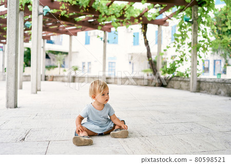 Little girl sitting on a tile in a patio entwined with grapes Little girl sitting on a tile in a patio entwined with grapes 80598521