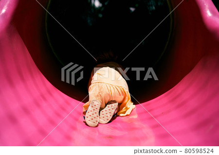 Little girl in a dress crawls into a pipe on the playground. Back view Little girl in a dress crawls into a pipe on the playground. Back view 80598524