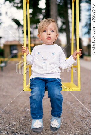 Child sits on a yellow swing in the playground 80598579