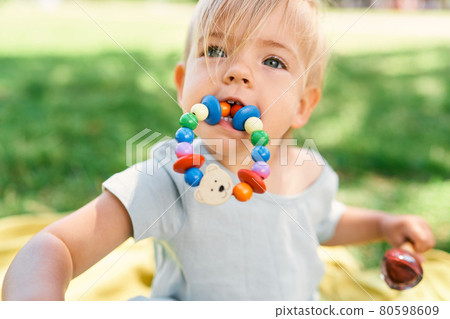 Little girl with a toy bracelet in her mouth holds an ice cream in her hand. Portrait 80598609
