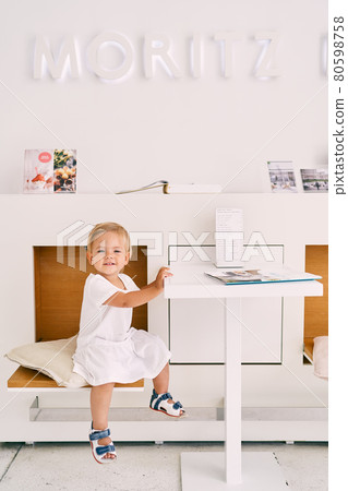 Little smiling girl sits in a cafe at a table on a chair 80598758
