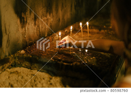 Woman puts a lighted candle on a candlestick Woman puts a lighted candle on a candlestick 80598760