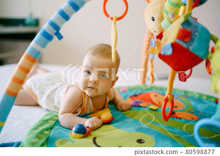 Baby lies on his stomach on a play mat and holds a rattle in his hand Baby lies on his stomach on a play mat and holds a rattle in his hand 80598877