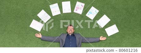 Happy businessman lies on green lawn in documents with business charts Happy businessman lies on green lawn in documents with business charts 80601216