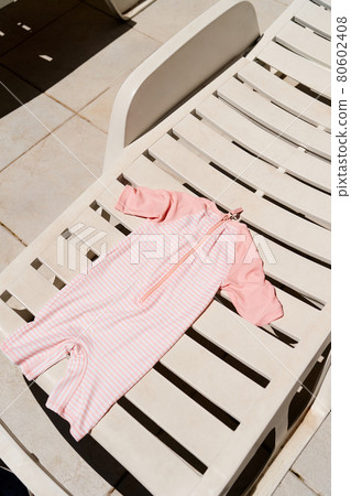 Children striped jumpsuit lies on a white sun lounger Children striped jumpsuit lies on a white sun lounger 80602408