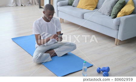 African Man using Smartphone on Yoga Mat at Home African Man using Smartphone on Yoga Mat at Home 80602959