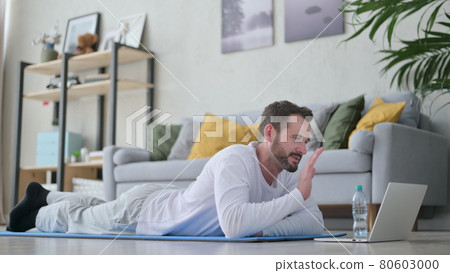 Mature Adult Man doing Video Call on Laptop while on Yoga Mat Mature Adult Man doing Video Call on Laptop while on Yoga Mat 80603000