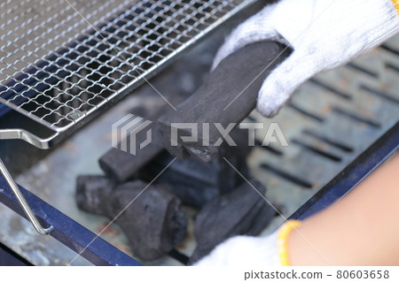 A woman's hand putting charcoal on the stove in preparation for barbecue A woman's hand putting charcoal on the stove in preparation for barbecue 80603658