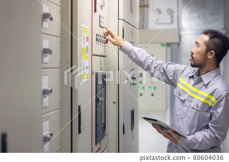 Engineer or technician man using tablet to monitor process, business, and industry concept in switch gear electrical room of oil and gas platform or plant industrial. 80604036
