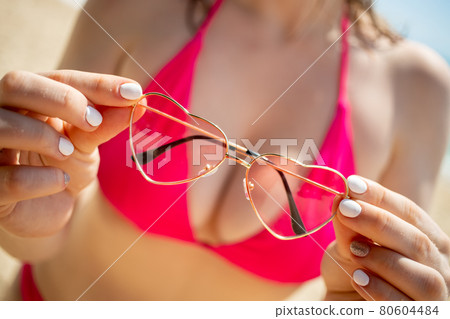 young woman in pink bikini holds sunglasses hearts on sea beach background 80604484