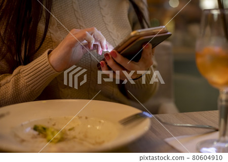 close-up of female hands holding a phone and typing in it in the evening in a cafe close-up of female hands holding a phone and typing in it in the evening in a cafe 80604910