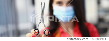 Woman hairdresser in medical protective mask holds scissors in hand Woman hairdresser in medical protective mask holds scissors in hand 80604911