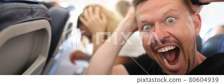 Male passenger holding his head and shouting on plane 80604939