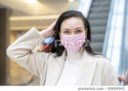 beautiful woman in a pink medical mask on her face against the background of the escadator in a public place beautiful woman in a pink medical mask on her face against the background of the escadator in a public place 80604942
