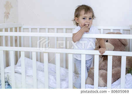 coronavirus covid-19 quarantine concept. take time with your family. little cute toddler is standing in the crib and looking at the camera smiling cheerfully 80605069