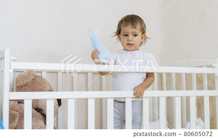 quarantine coronavirus covid-19 pandemic concept. a little cute serious baby is in a baby cot at home in safety and holding a medical mask. copy space 80605072