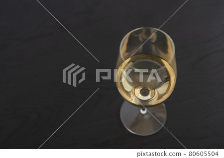 White wine in a wineglass on black oak table with copy space 80605504