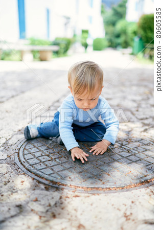 Kid sits on a metal hatch in the yard 80605585
