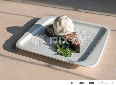 Chocolate brownie with an ice cream on a white plate on a wooden table. 80609208