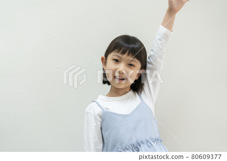 A second grade girl with one hand raised, looking at the camera, portrait 80609377